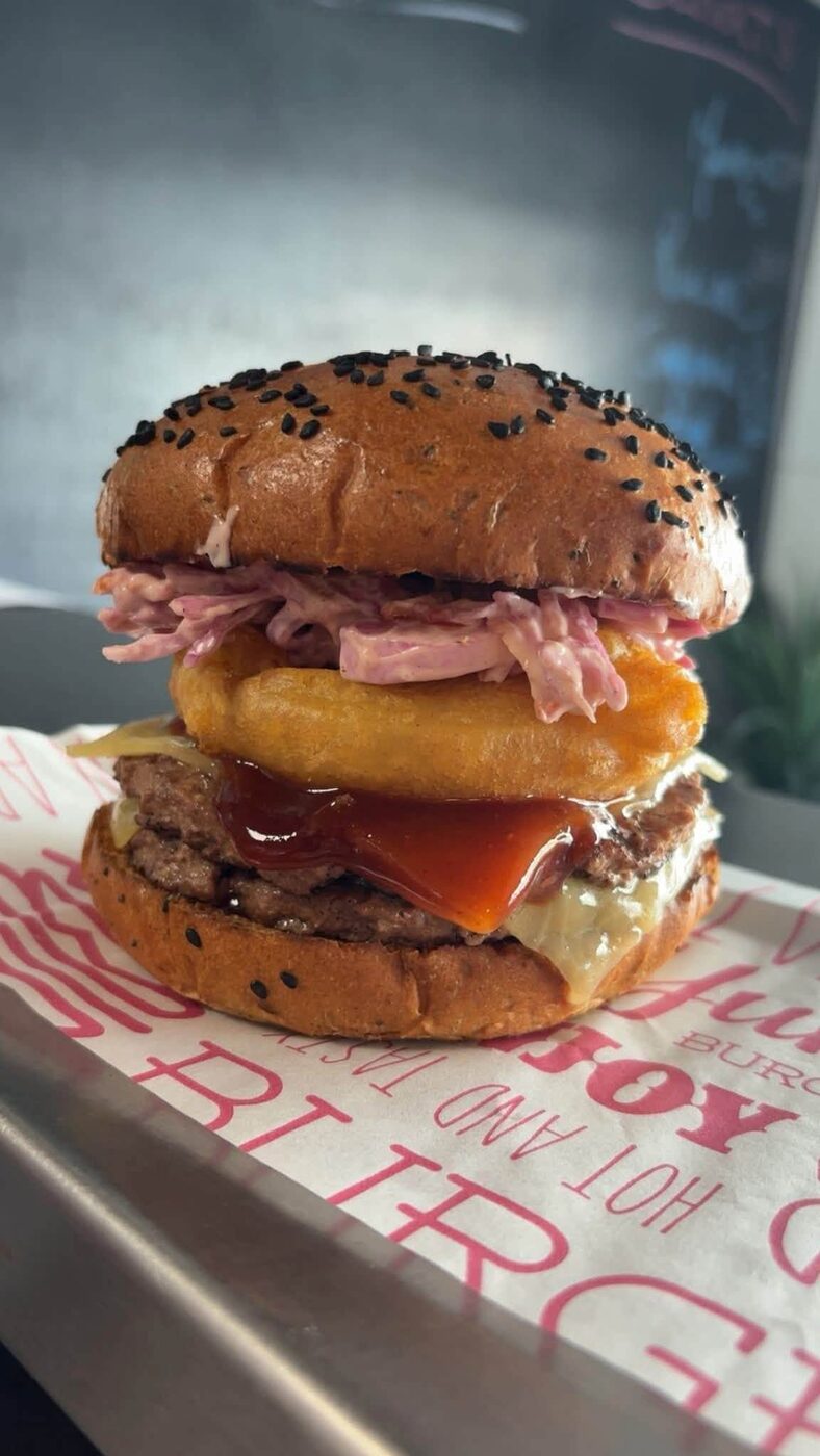 A stacked steak burger with onion ring, coleslaw and BBQ sauce